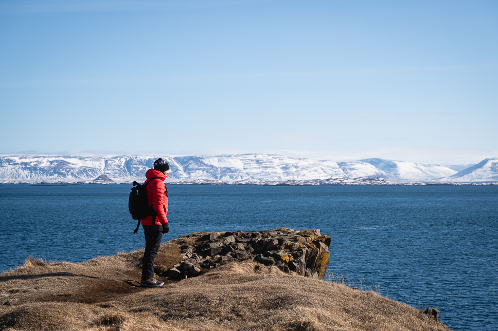 Man in de winter in IJsland uitkijkend over de zee en besneeuwde bergen met een fotografie rugzak van Lowepro