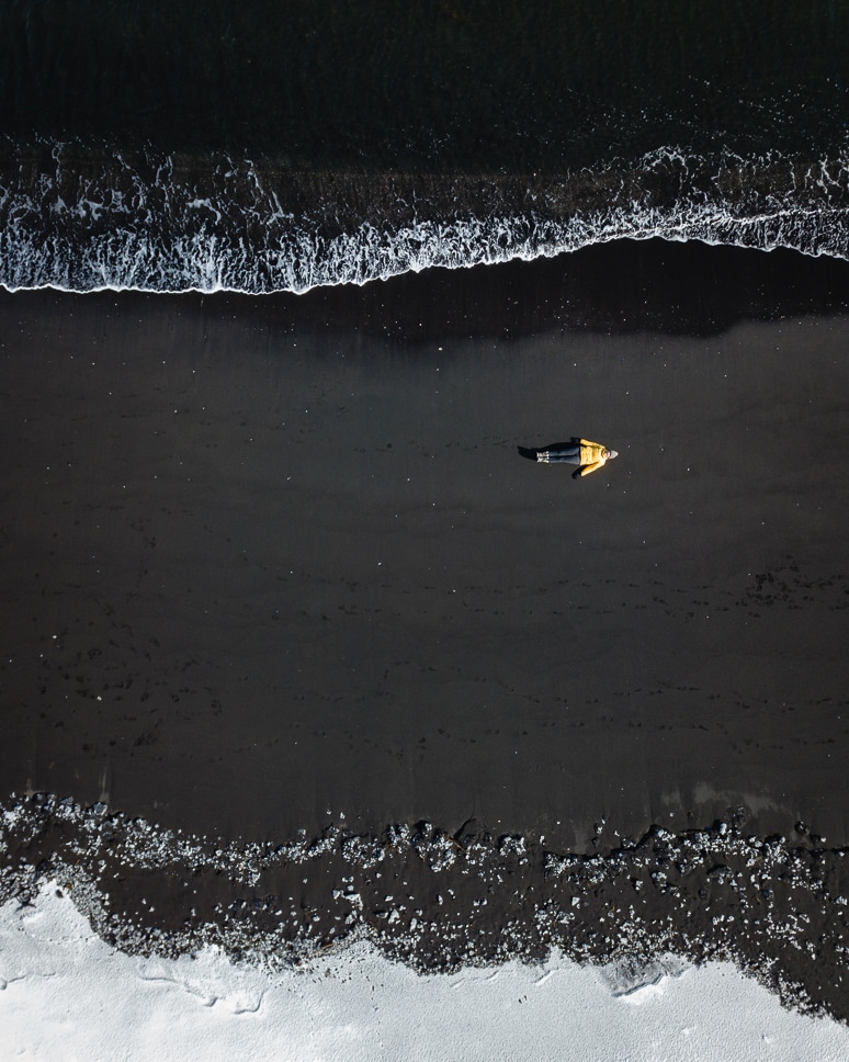 drone picture of a woman on a black beach at hvitserkur in iceland