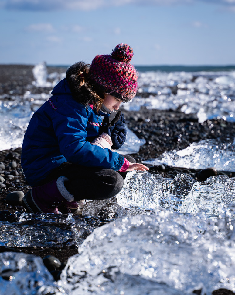 20+ Best things to do in Iceland: Our Ultimate Iceland Bucket List Girl in winter touches the ice blocks on Diamond Beach in Iceland that lie glittering in the sun on the black sand
