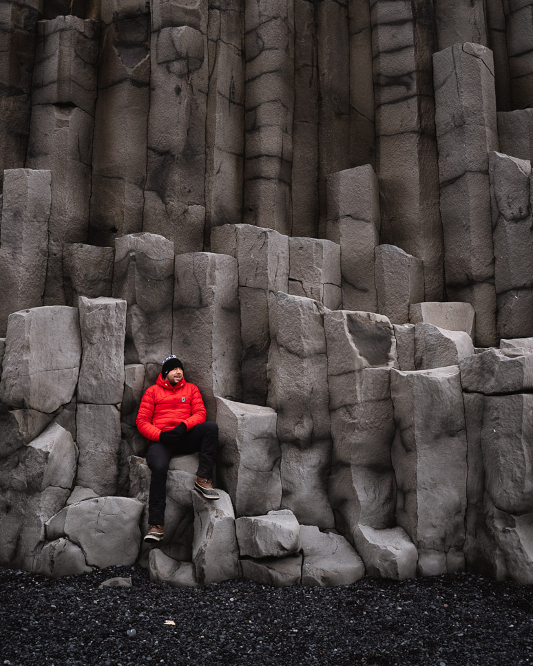 men with red jacket on grey basalt black beach ring road iceland