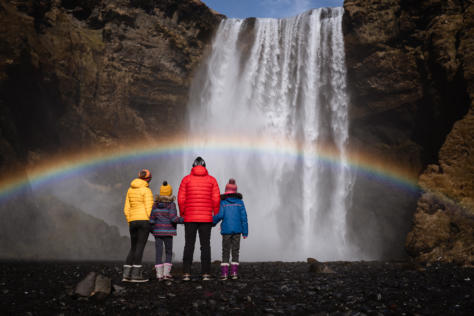 20+ Best things to do in Iceland: Our Ultimate Iceland Bucket List Family watching Skogafoss waterfall with rainbow in South Iceland, one of the most beautiful sights in Iceland