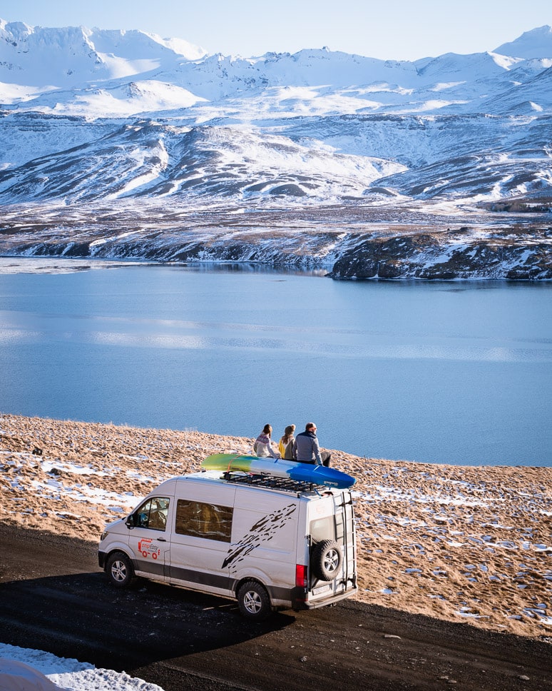 father with kids sitting on a roof of camper watching mountains in iceland