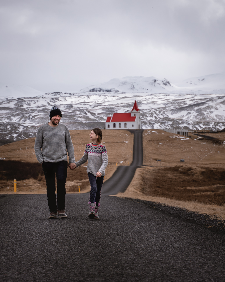 What to wear in Iceland in winter: the best clothing for Iceland from October to April father and daughter walking away from a church in winter in iceland, dressed in woolen sweaters and winter clothing