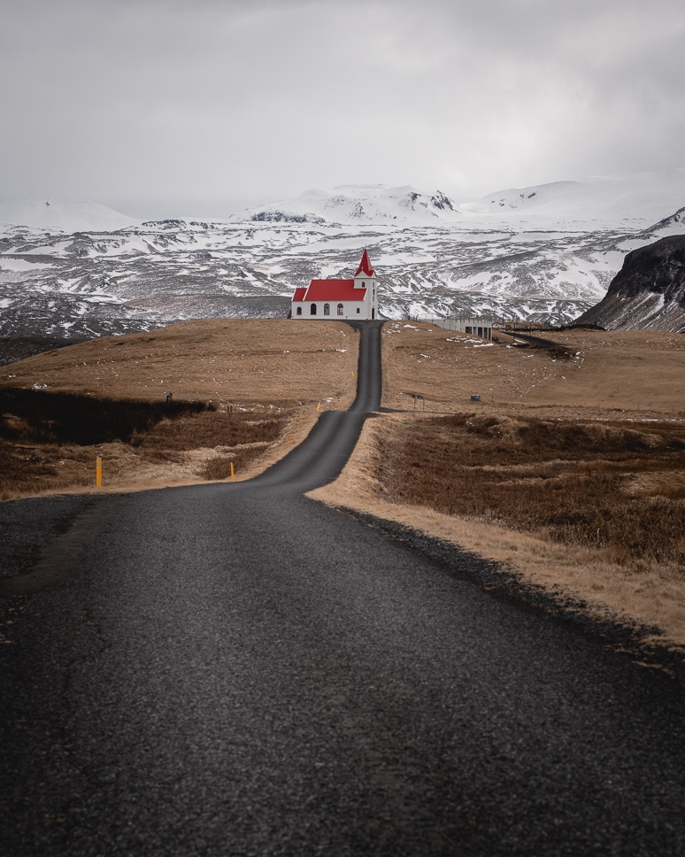 20+ Best things to do in Iceland: Our Ultimate Iceland Bucket List A road leading to Ingjaldshólskirkja, a white church with a red roof and snow-capped mountains on the Snaefellsnes peninsula