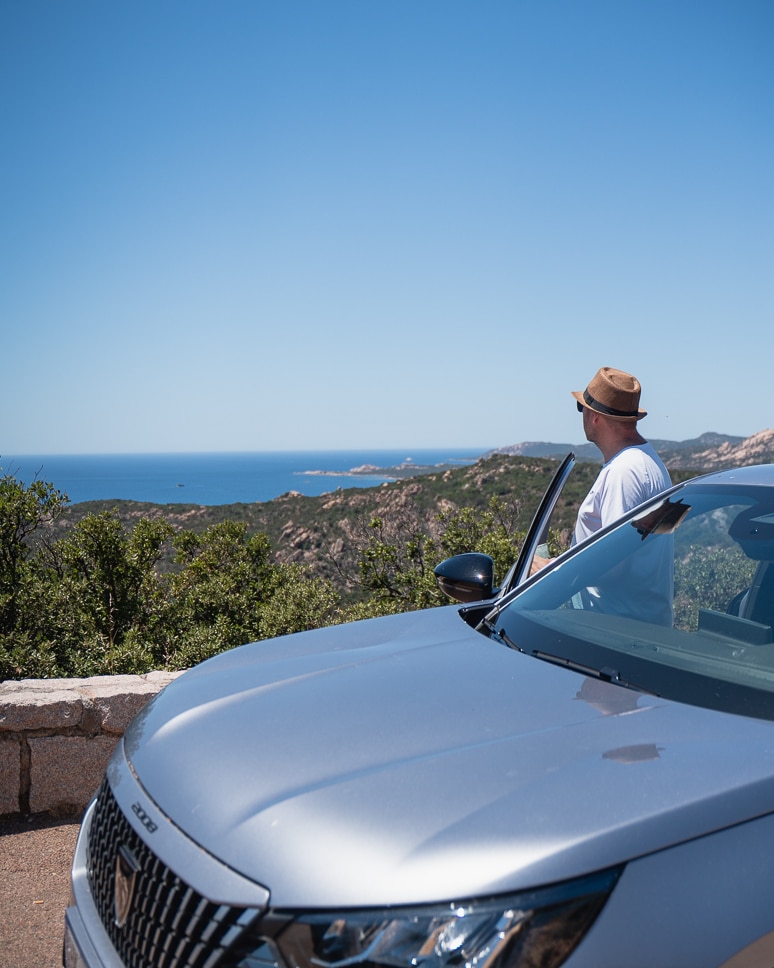 Car rental in Corsica: everything you need to know (+ our own experience driving in Corsica) Man looking out over the beaches from the car during a road trip in Corsica